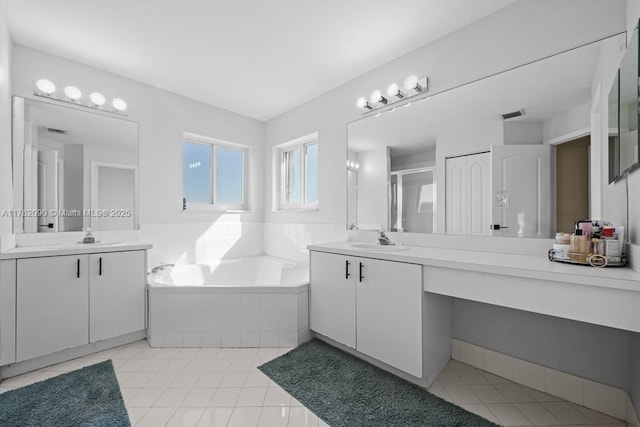 bathroom featuring a bath, tile patterned floors, two vanities, and a sink