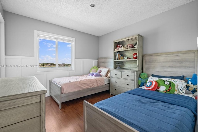 bedroom featuring a textured ceiling, dark wood finished floors, and wainscoting