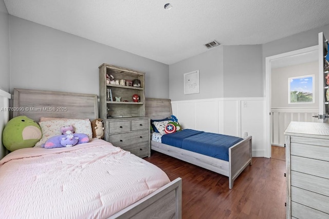 bedroom with visible vents, wainscoting, a textured ceiling, and wood finished floors