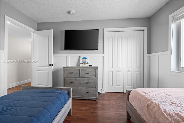 bedroom with a closet, wainscoting, a textured ceiling, and dark wood-type flooring