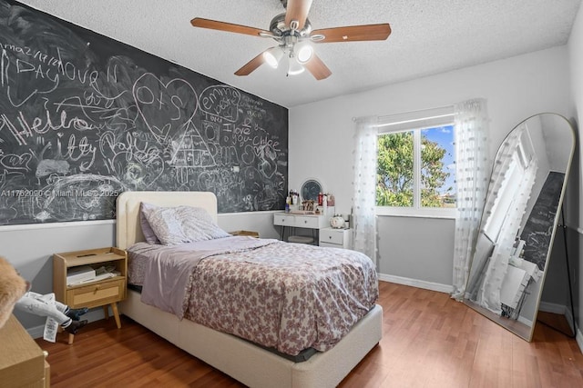 bedroom with a ceiling fan, wood finished floors, baseboards, and a textured ceiling