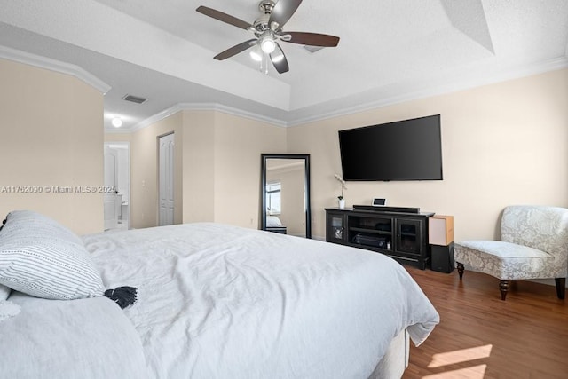 bedroom featuring visible vents, ornamental molding, a ceiling fan, a tray ceiling, and wood finished floors