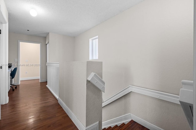 hallway with a textured ceiling, baseboards, and wood finished floors