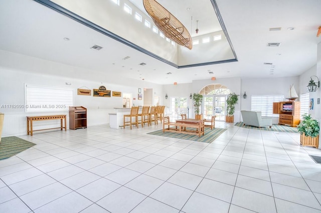 unfurnished living room with light tile patterned floors, visible vents, and a high ceiling