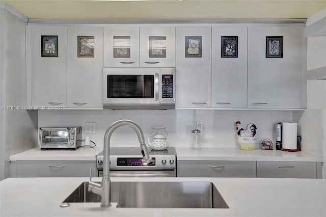 kitchen featuring a toaster, stainless steel microwave, gray cabinetry, and light countertops