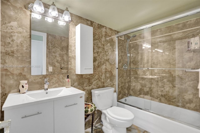 bathroom with combined bath / shower with glass door, toilet, tile walls, and vanity