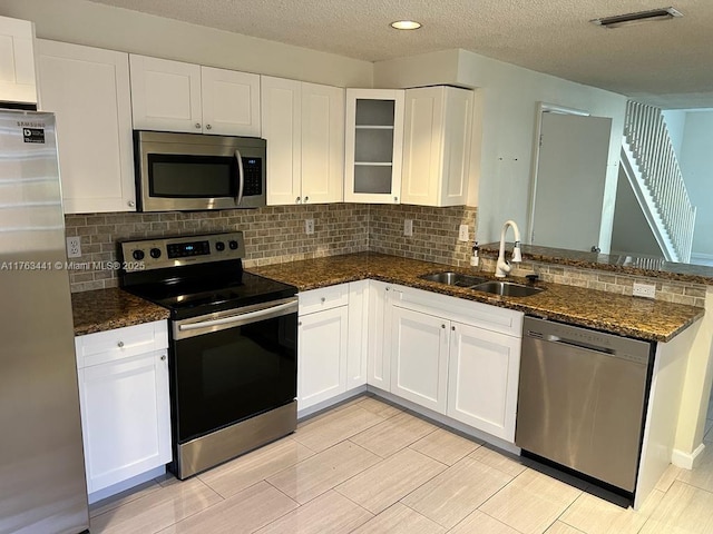 kitchen featuring visible vents, a peninsula, a sink, appliances with stainless steel finishes, and white cabinetry