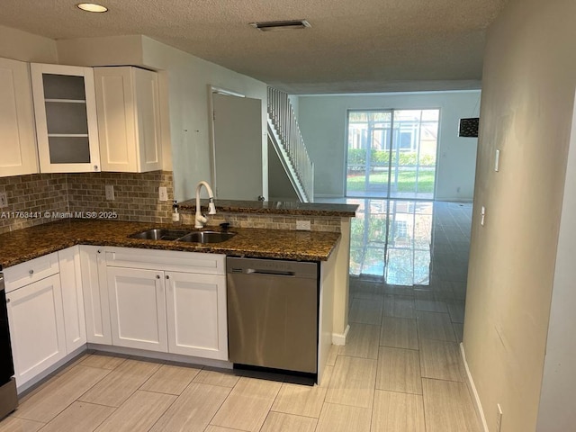 kitchen featuring visible vents, a sink, stainless steel dishwasher, a peninsula, and white cabinets