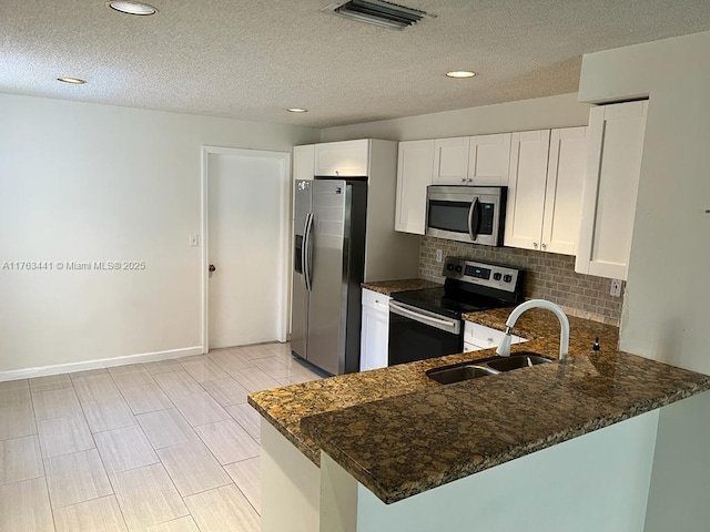 kitchen with visible vents, dark stone countertops, a peninsula, stainless steel appliances, and a sink