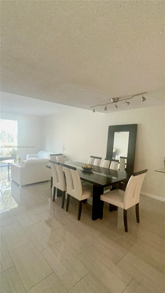 dining space featuring baseboards, a textured ceiling, and track lighting