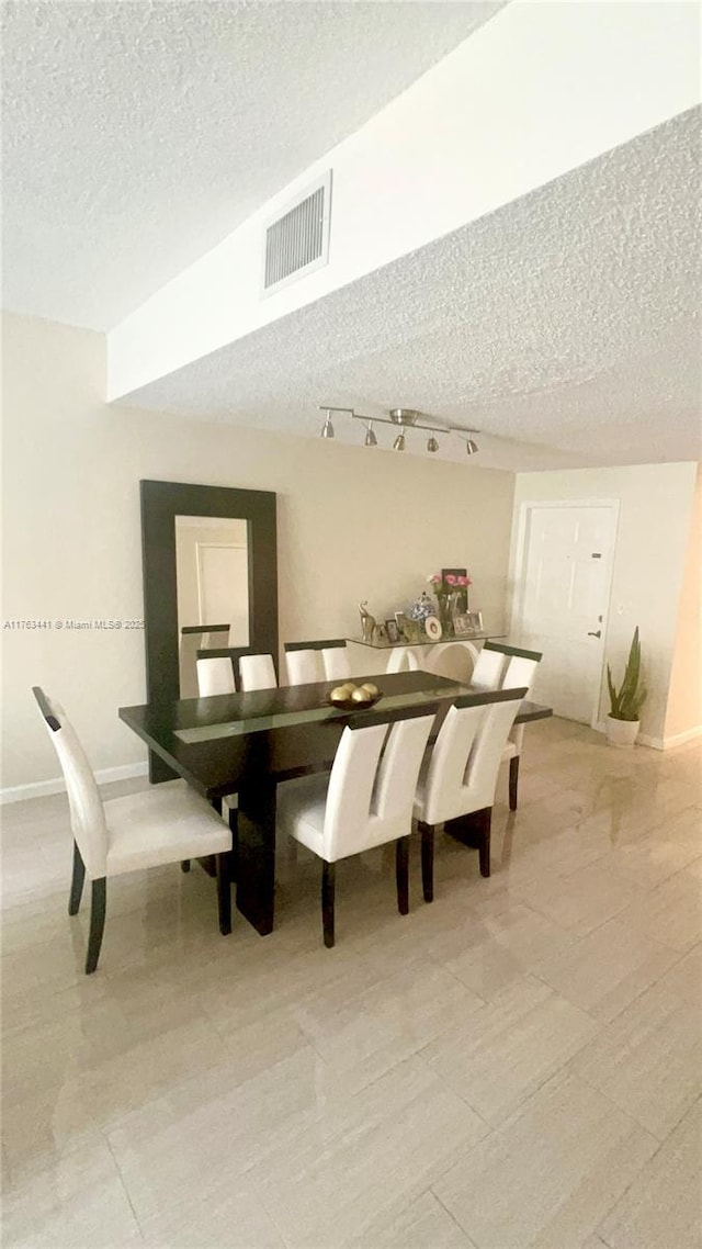 dining room with rail lighting, baseboards, visible vents, and a textured ceiling