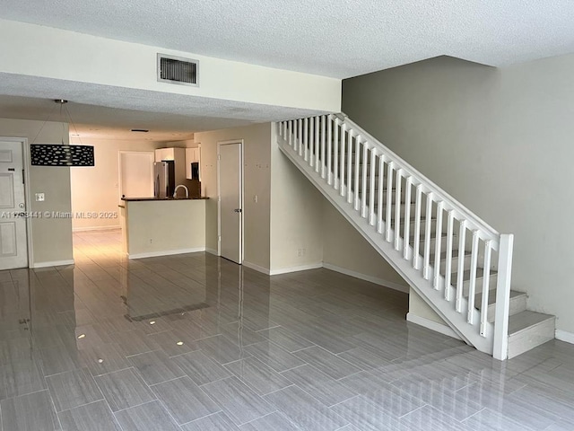 stairs with wood finish floors, visible vents, baseboards, and a textured ceiling