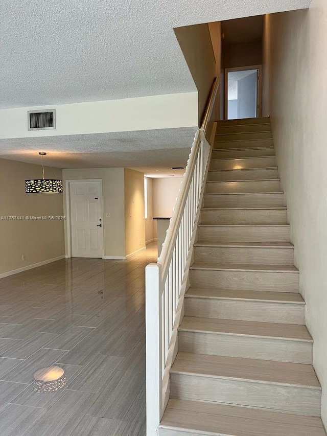 staircase featuring visible vents, a textured ceiling, and baseboards