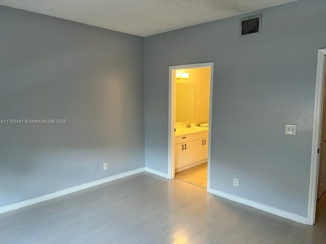 unfurnished room featuring visible vents, wood finished floors, baseboards, and a sink