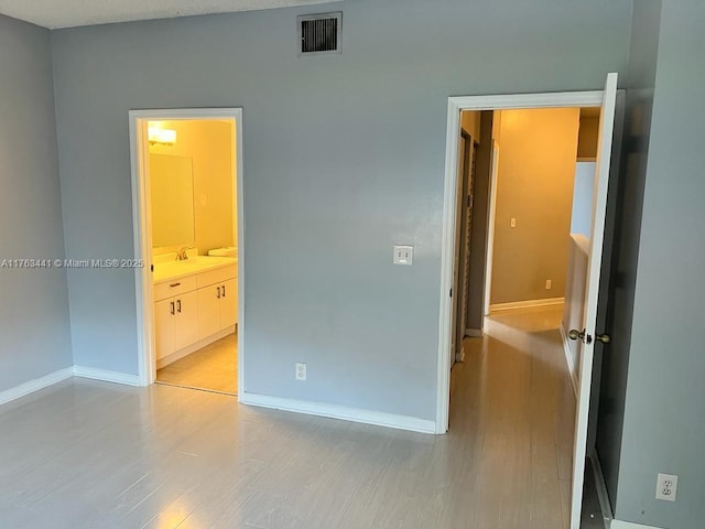 unfurnished bedroom featuring a sink, baseboards, visible vents, and light wood-type flooring