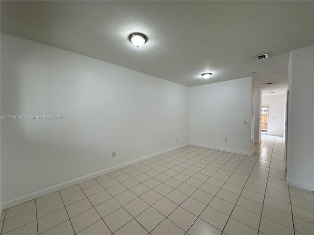 empty room with light tile patterned floors, visible vents, a textured ceiling, and baseboards