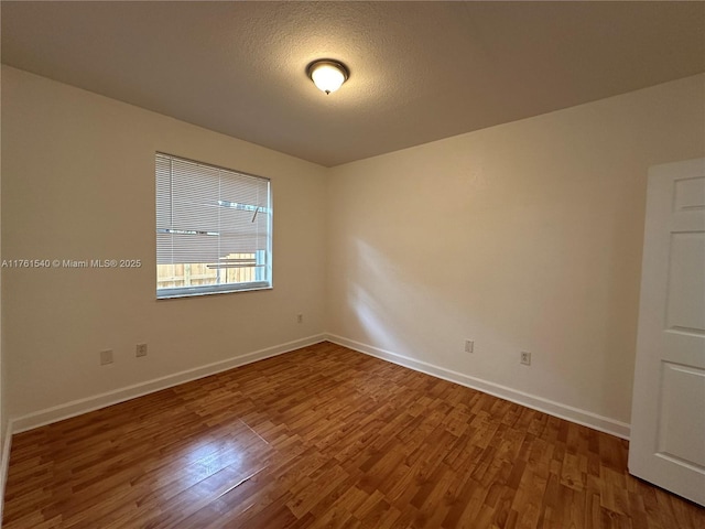 unfurnished room with a textured ceiling, baseboards, and wood finished floors