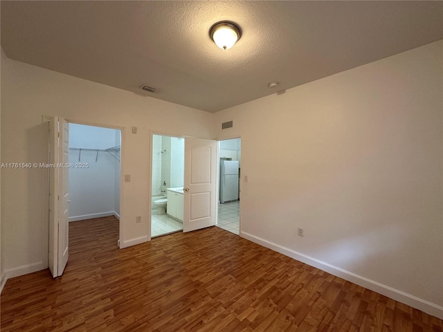 unfurnished bedroom featuring visible vents, wood finished floors, freestanding refrigerator, a closet, and a spacious closet