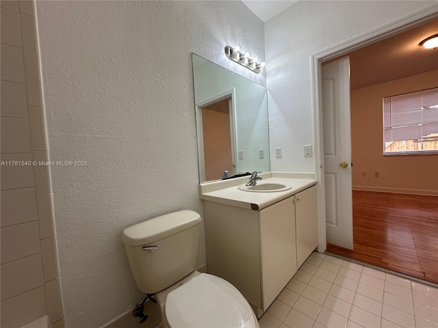 bathroom featuring tile patterned flooring, toilet, vanity, and a textured wall