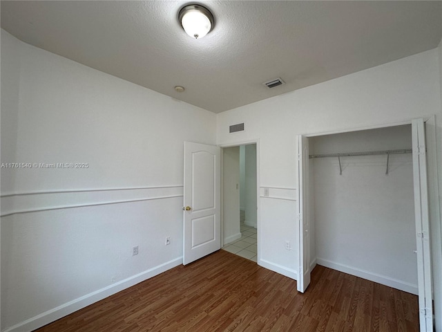 unfurnished bedroom featuring visible vents, baseboards, a closet, and wood finished floors