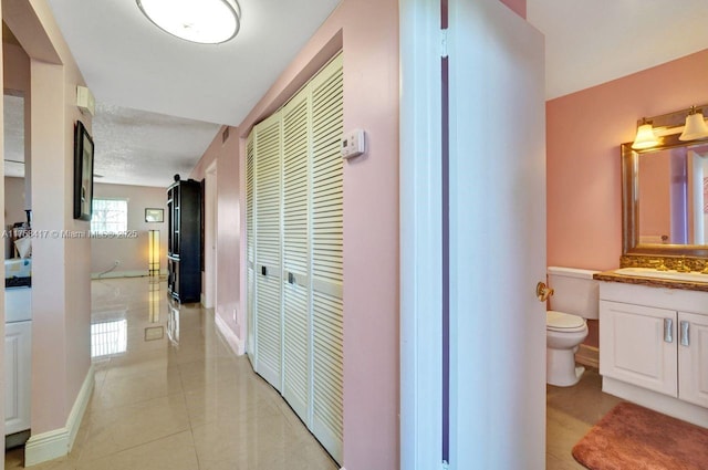 hall featuring light tile patterned flooring, baseboards, and a sink