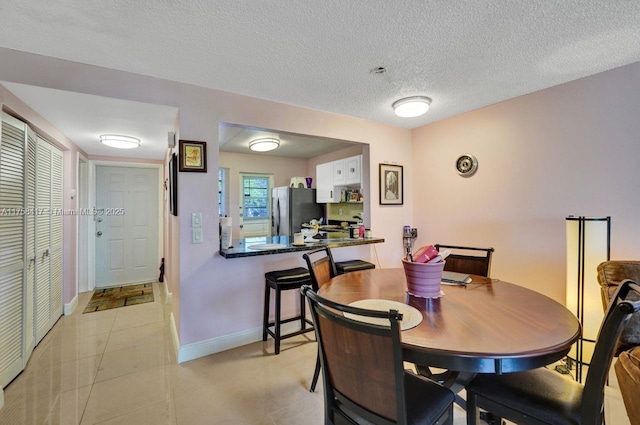 dining room with light tile patterned flooring, a textured ceiling, and baseboards