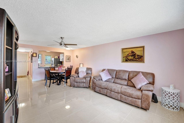 living area with light tile patterned floors, a ceiling fan, baseboards, and a textured ceiling