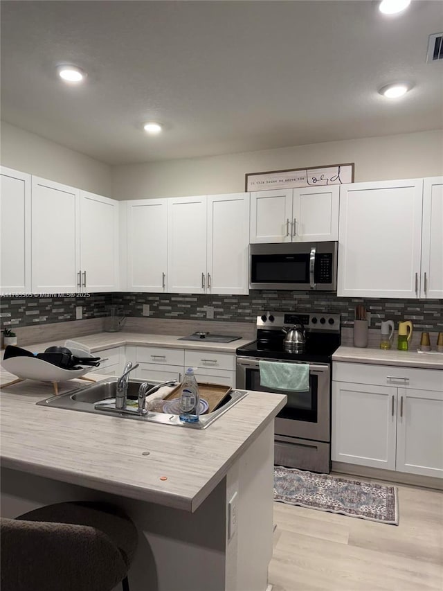 kitchen featuring a sink, tasteful backsplash, white cabinetry, stainless steel appliances, and light countertops