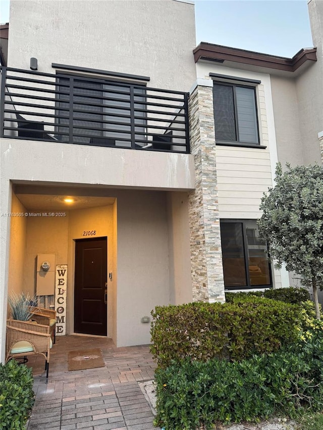 entrance to property featuring stone siding, stucco siding, and a balcony