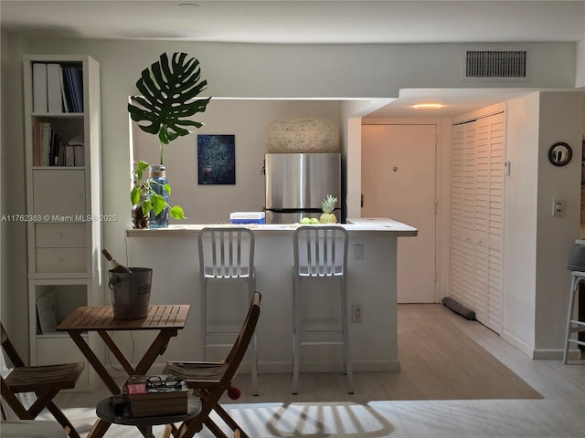 kitchen featuring light wood-type flooring, visible vents, a kitchen bar, and freestanding refrigerator