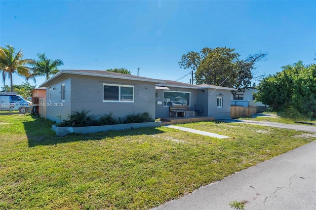 ranch-style home with stucco siding, a front yard, and fence