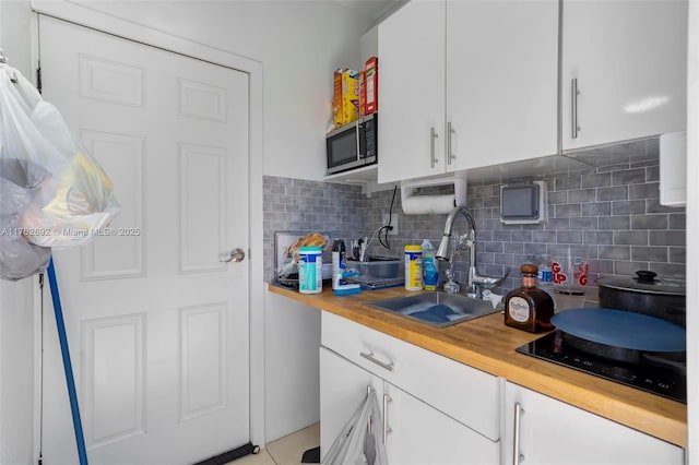 kitchen with a sink, white cabinetry, stainless steel microwave, black electric stovetop, and tasteful backsplash