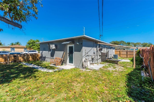 rear view of house featuring a fenced backyard, central air condition unit, stucco siding, and a yard