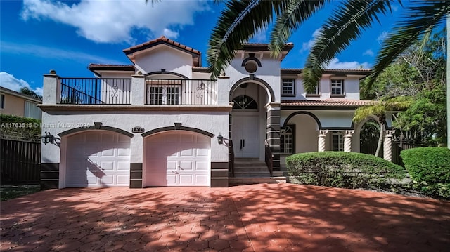 mediterranean / spanish house featuring a balcony, an attached garage, stucco siding, a tiled roof, and decorative driveway