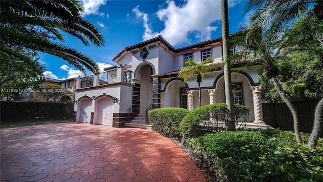 mediterranean / spanish-style home featuring stucco siding, decorative driveway, fence, an attached garage, and a balcony