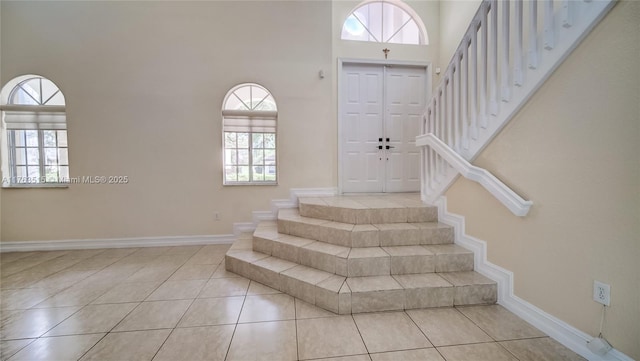 stairs featuring tile patterned floors, baseboards, and a towering ceiling