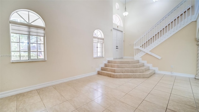 tiled foyer entrance with stairs, baseboards, and a towering ceiling