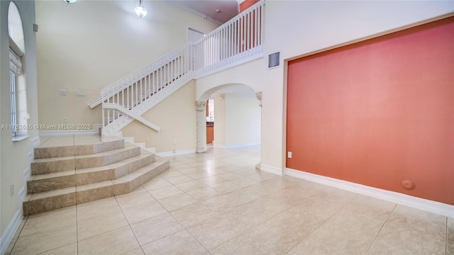 stairway with tile patterned floors, baseboards, arched walkways, and a high ceiling