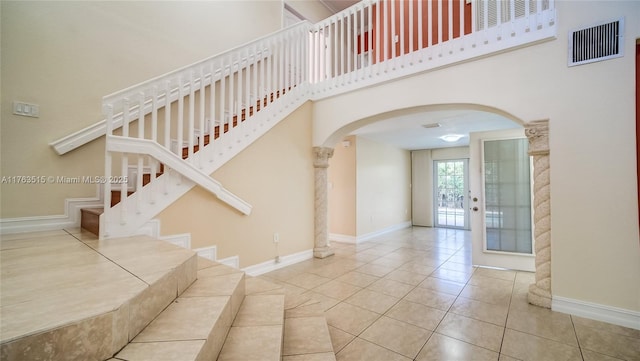 stairway featuring visible vents, arched walkways, a high ceiling, tile patterned flooring, and baseboards