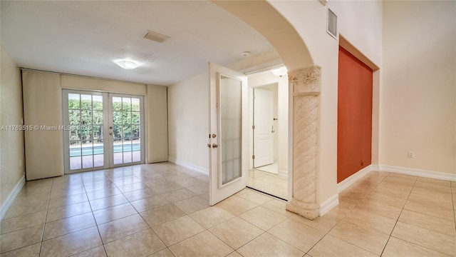 empty room with visible vents, french doors, arched walkways, light tile patterned floors, and baseboards