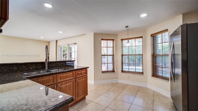 kitchen featuring a sink, freestanding refrigerator, dark stone counters, light tile patterned floors, and hanging light fixtures