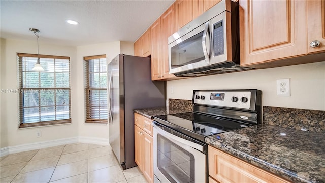 kitchen with baseboards, light brown cabinetry, light tile patterned floors, dark stone countertops, and appliances with stainless steel finishes