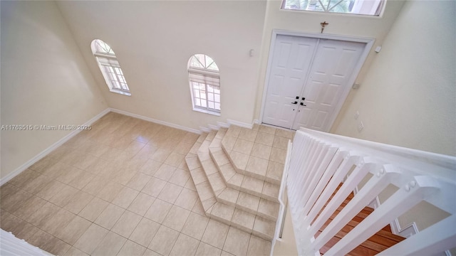 foyer entrance featuring light tile patterned floors, baseboards, and a towering ceiling