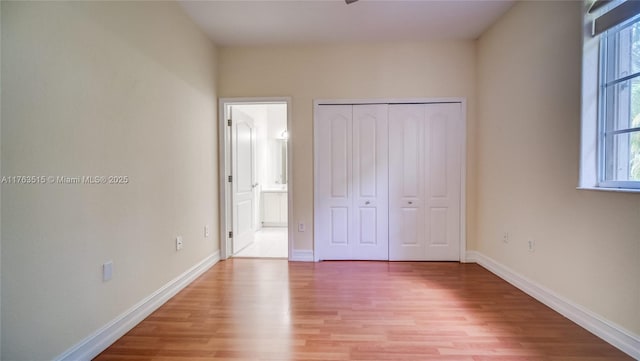 unfurnished bedroom with a closet, multiple windows, light wood-style flooring, and baseboards