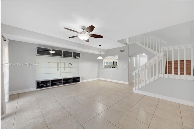 unfurnished living room featuring stairs, visible vents, baseboards, and ceiling fan