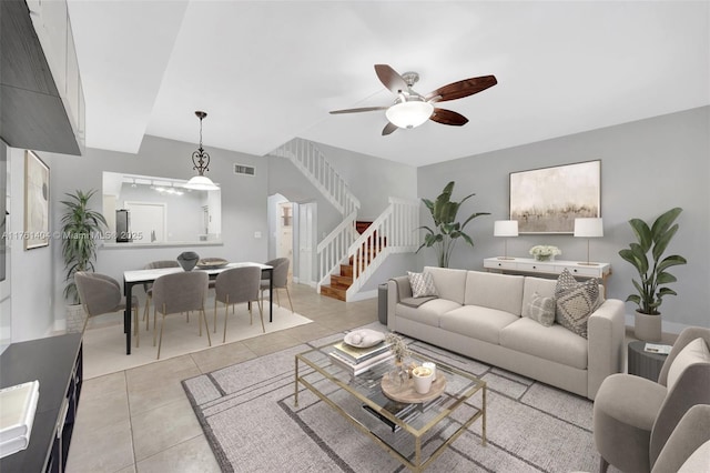 living room with stairway, visible vents, light tile patterned flooring, and a ceiling fan