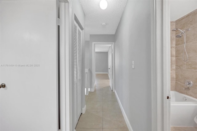 hallway featuring light tile patterned floors, a textured ceiling, and baseboards