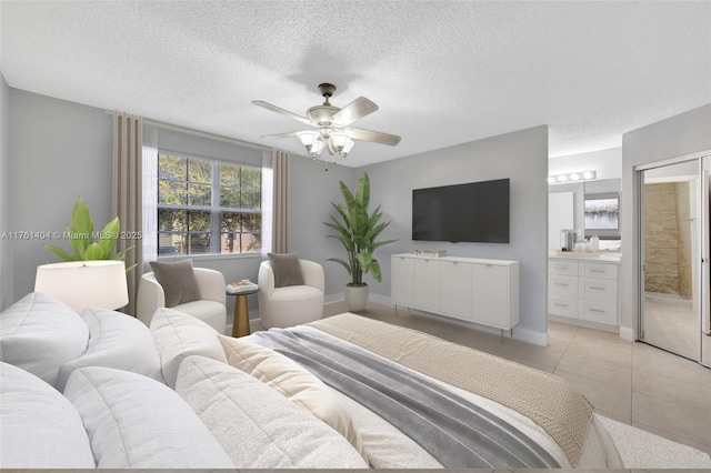 bedroom featuring baseboards, ceiling fan, light tile patterned floors, ensuite bathroom, and a textured ceiling