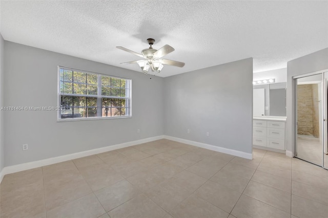 unfurnished bedroom featuring a textured ceiling, ensuite bath, light tile patterned flooring, baseboards, and ceiling fan