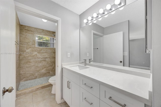 bathroom featuring tile patterned floors, toilet, a textured ceiling, tiled shower, and vanity